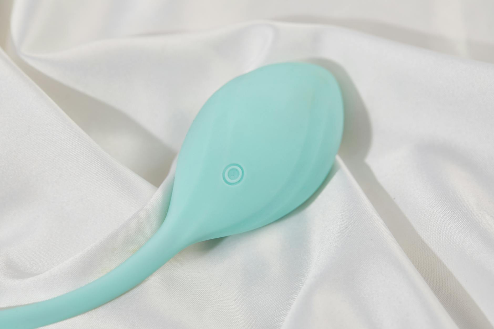A sleek teal clitoral vibrator resting on white silk, showcasing modern design