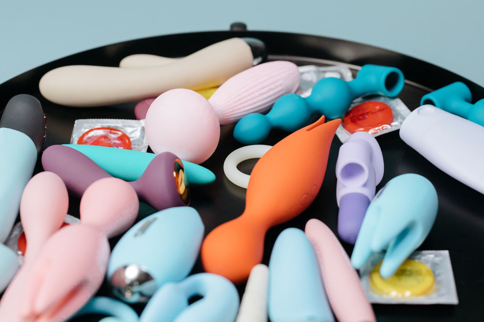 A colorful array of vibrators and adult toys on a black tray, representing diverse pleasure options