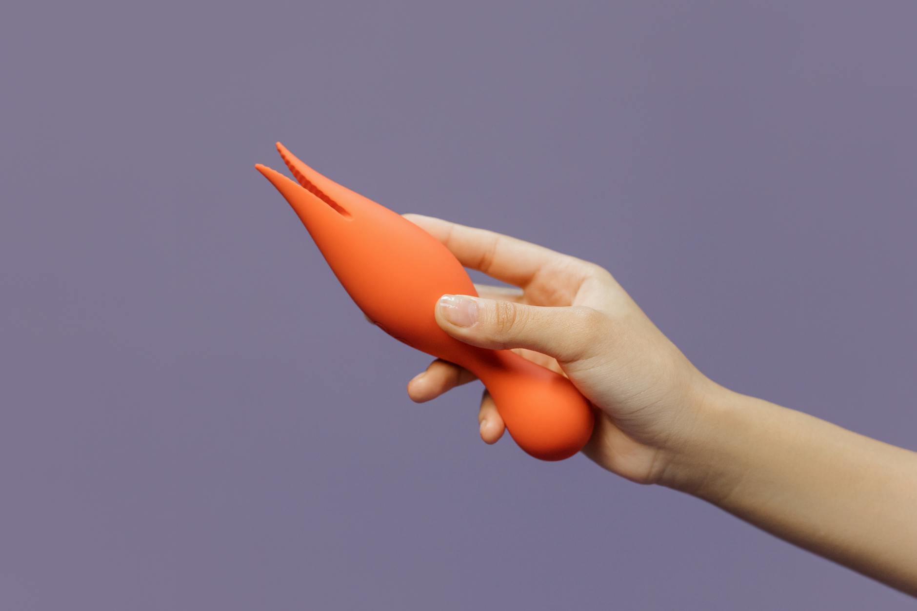 A hand holding a modern clitoral vibrator against a minimalist backdrop, representing intimate reconnection.