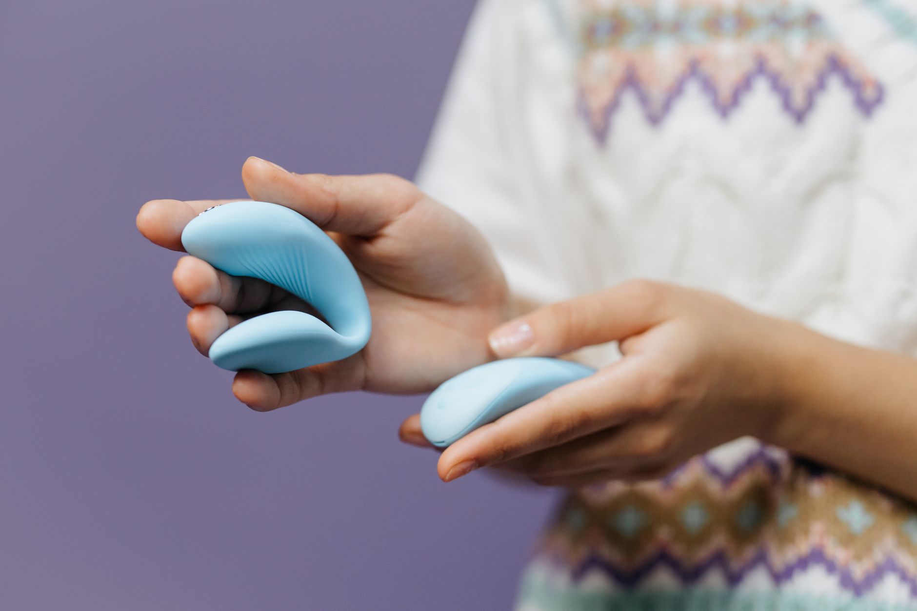 Close-up of a hand holding a blue lemon clitoral vibrator against a purple background